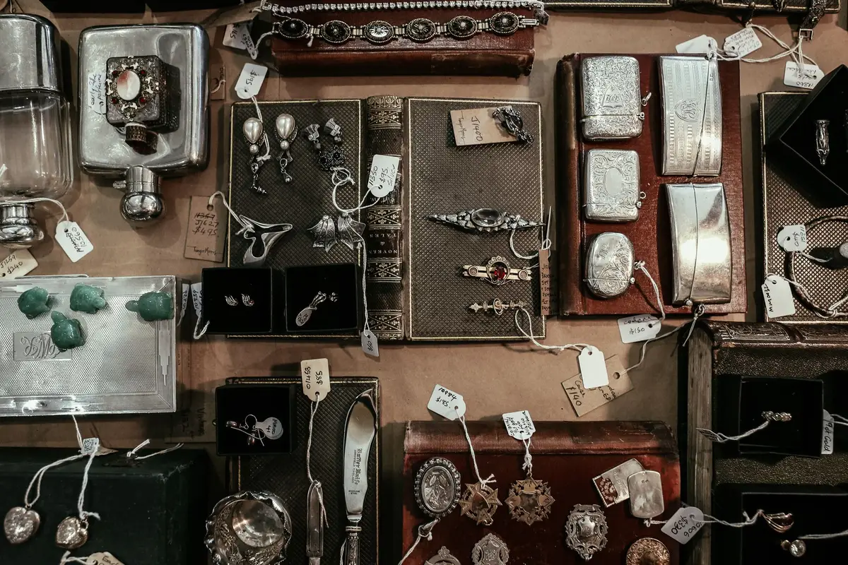 Antique silver cases, jewelry and small collectibles laid out on a table, each with a paper tag tied on