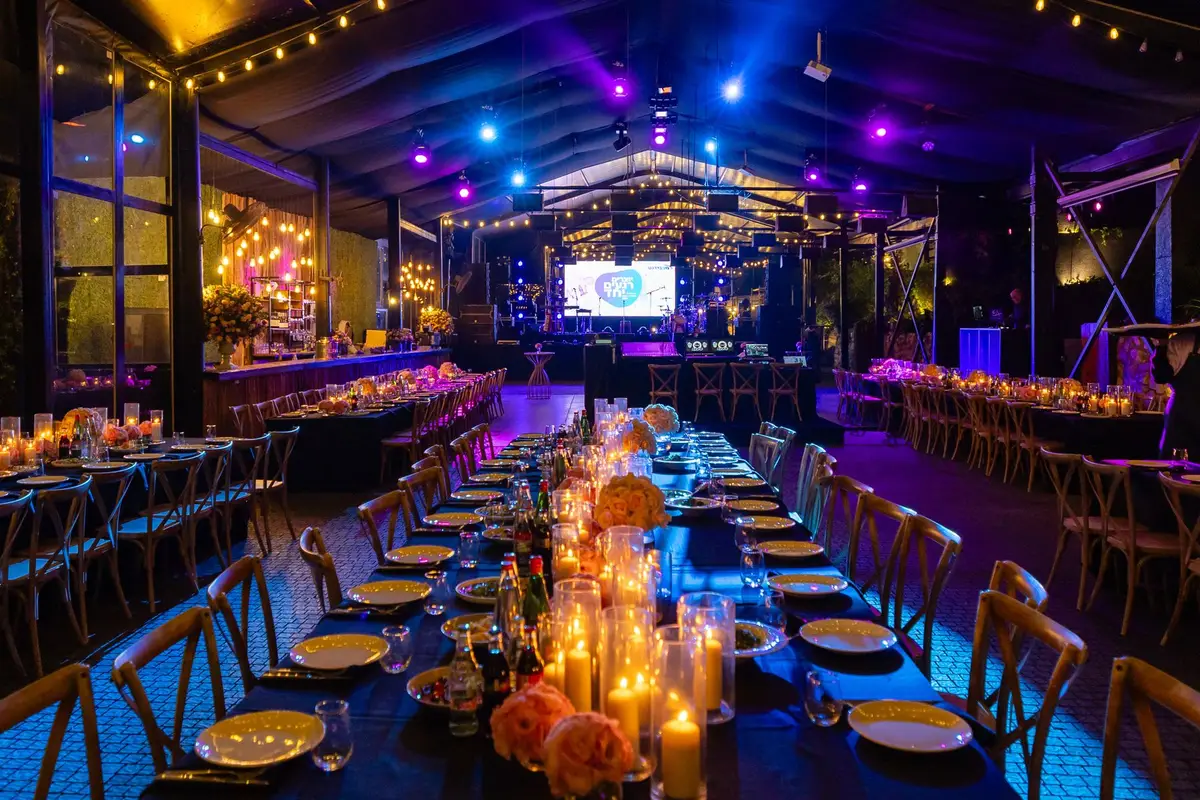 A gala venue set with long candlelit dinner tables under colored stage lighting before guests arrive