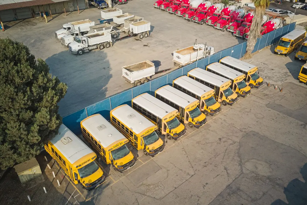 Aerial view of yellow school buses and white service trucks parked in rows in a fleet yard